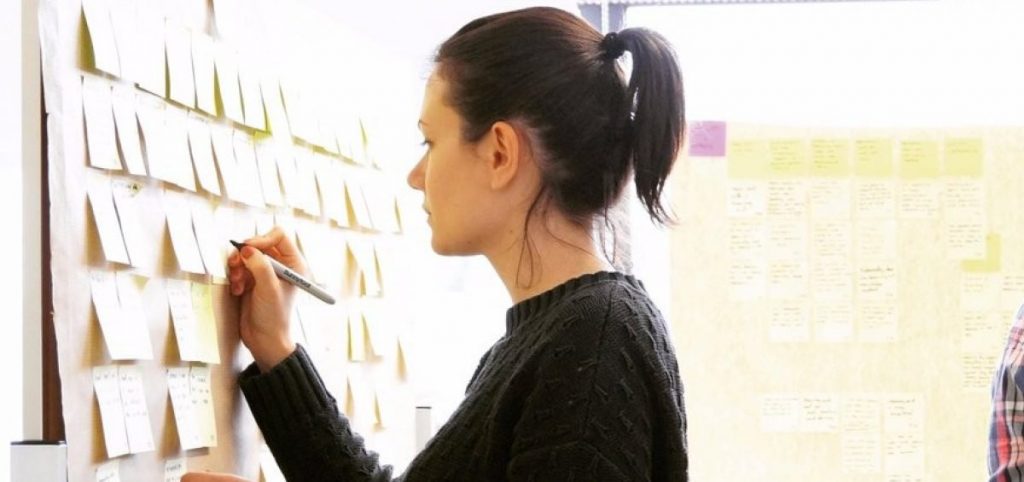 Image of a women writing on a wall that is full of post its. 