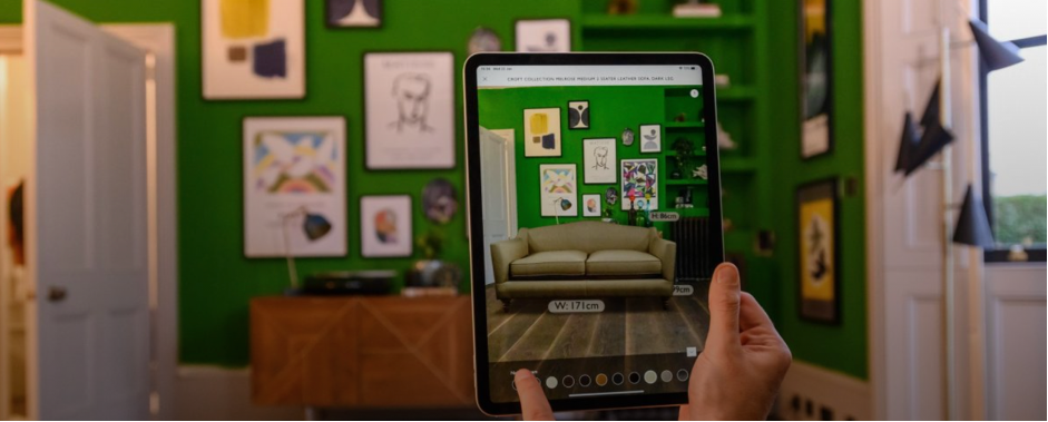 Image showing a hand that holds a tablet using AR to see if the sofa fits in the room. 
