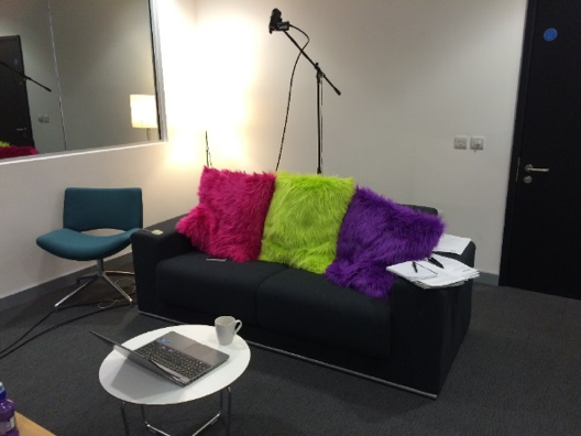 Image of a sofa with three colourful cushions. In front of the sofa is a table with a laptop and a cup